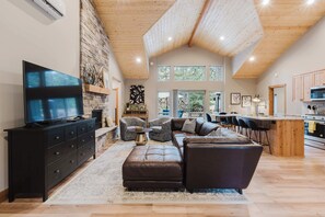 A spacious living area with a stone fireplace, a large flat-screen TV, and a cozy seating arrangement. - Luxury Pines Retreat at Black Butte Ranch (Sisters)