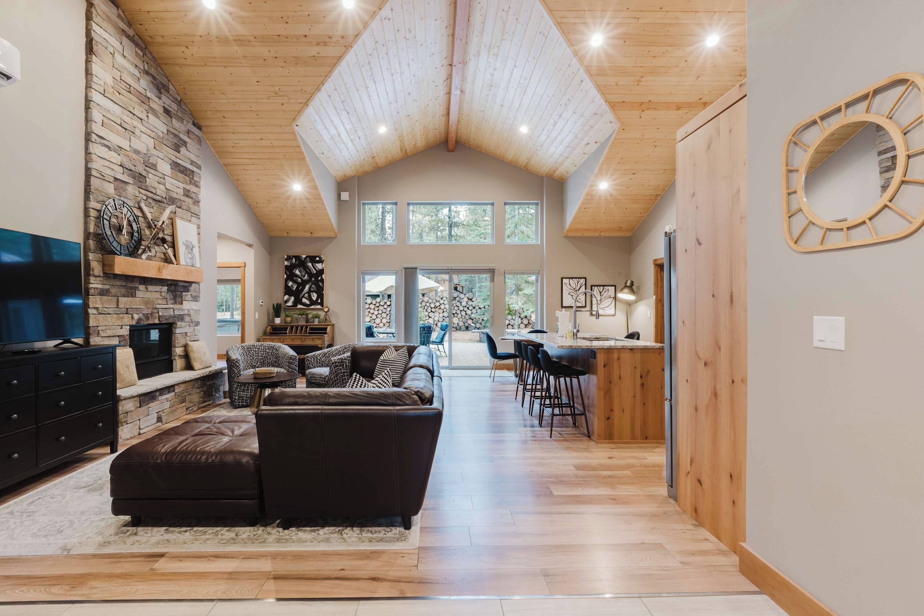 A spacious living area with a stone fireplace, leather sofa, and a dining area with a wooden ceiling.