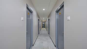 Um corredor com portas em ambos os lados, piso ladrilhado e teto com iluminação embutida.