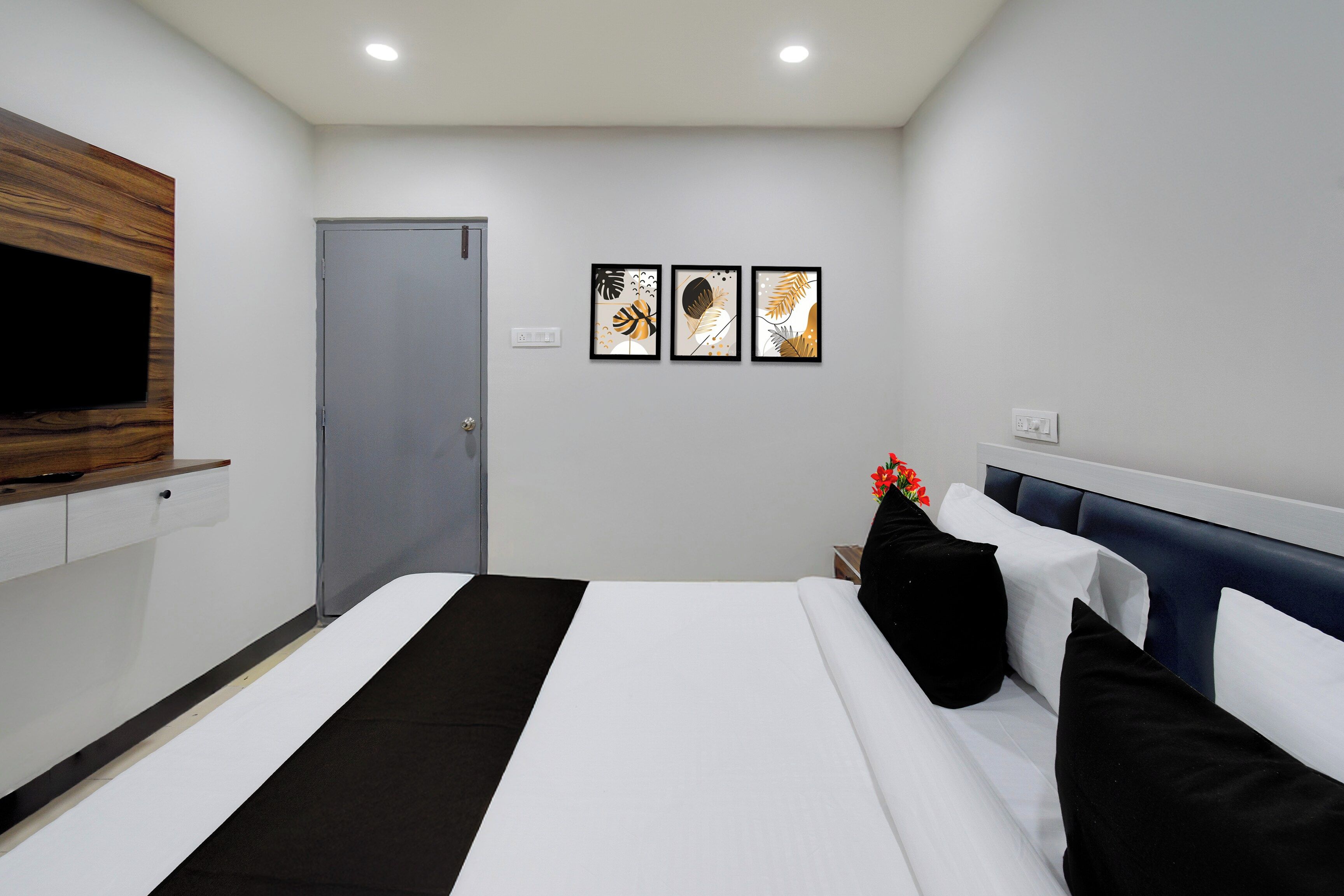 Habitación de hotel con una cama, un televisor montado en la pared, una puerta y tres cuadros enmarcados.