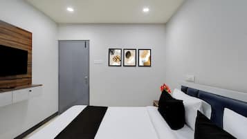 Habitación de hotel con una cama, un televisor montado en la pared, una puerta y tres cuadros enmarcados.
