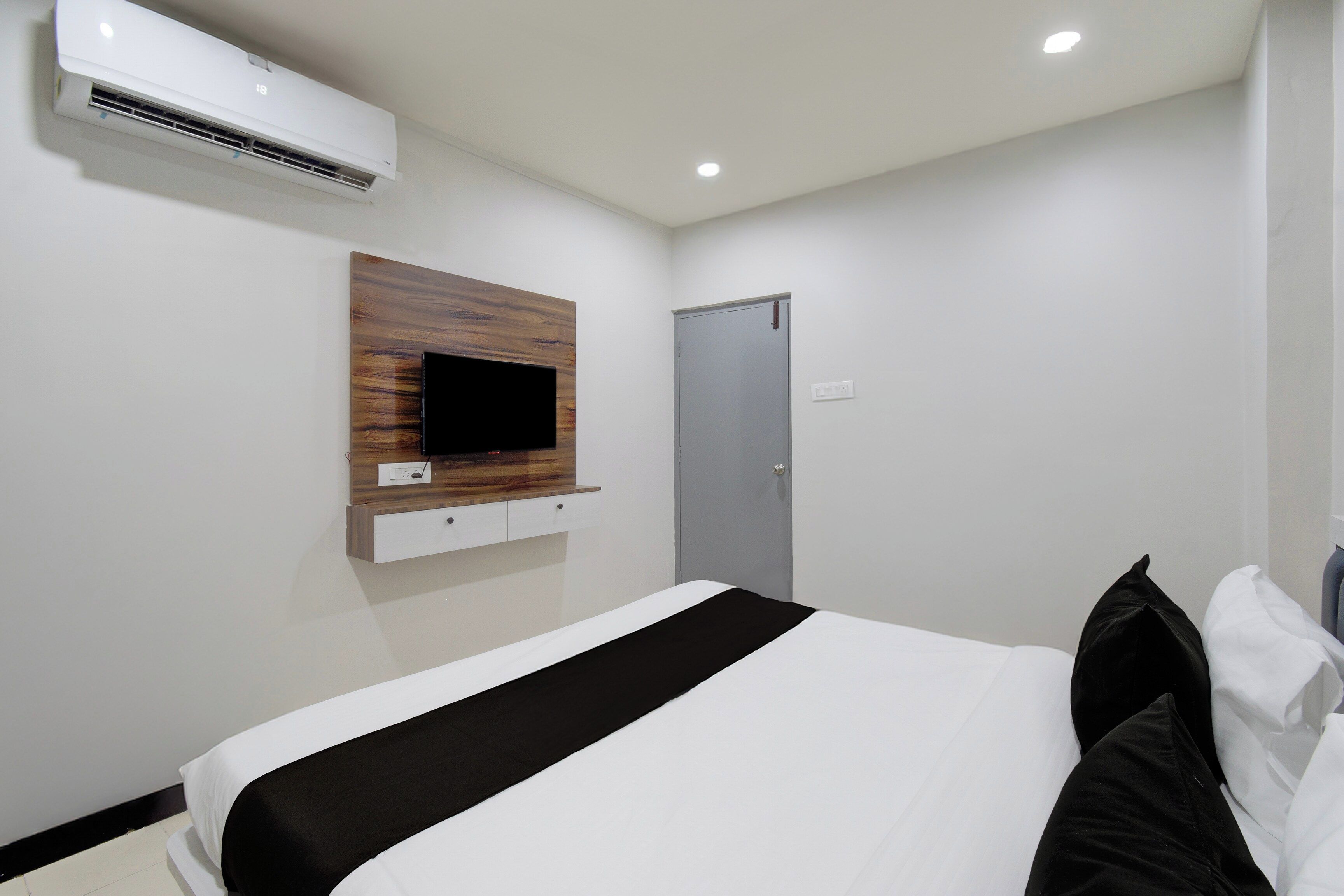 Una habitación de hotel con una cama, televisor montado, aire acondicionado y una puerta.