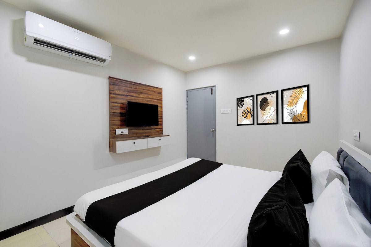 A hotel room with a bed, a mounted TV, an air conditioner, a door, and three framed artworks on the wall.