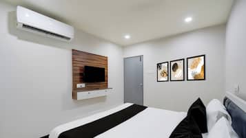 Habitació d'hotel amb un llit, un televisor penjat, aire condicionat, una porta i tres quadres al mur.