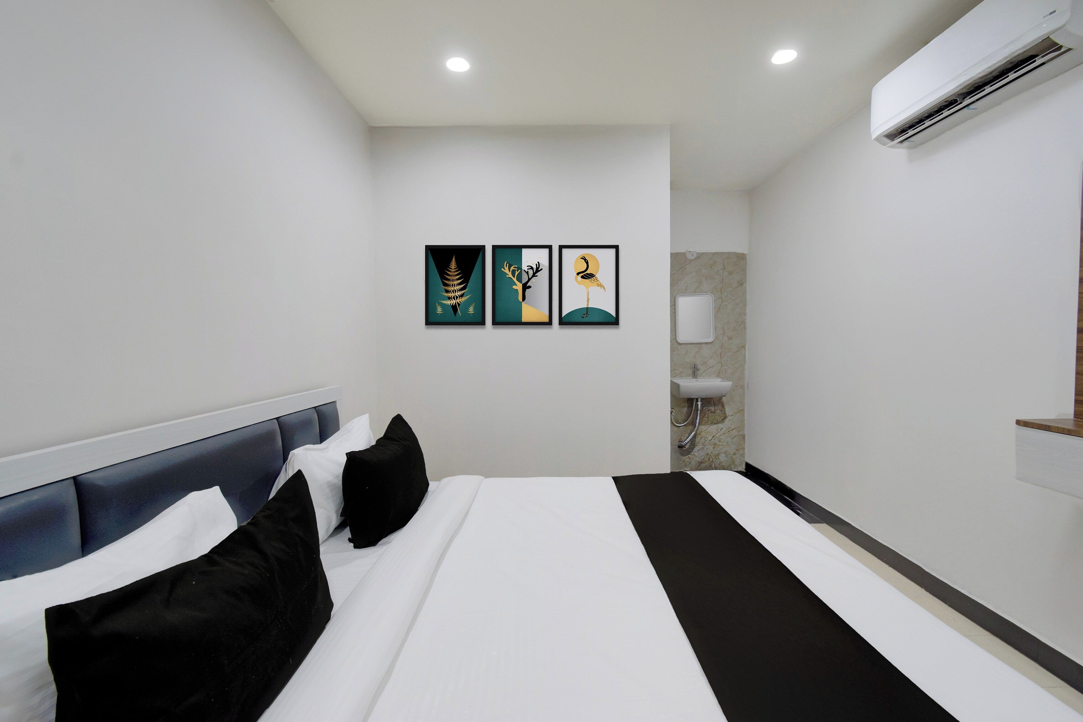Una camera d'albergo con un letto, una testiera, un condizionatore d'aria a muro e tre opere d'arte incorniciate.