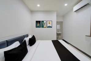 Una habitación de hotel con una cama, cabecera, aire acondicionado instalado en la pared y tres obras de arte enmarcadas.