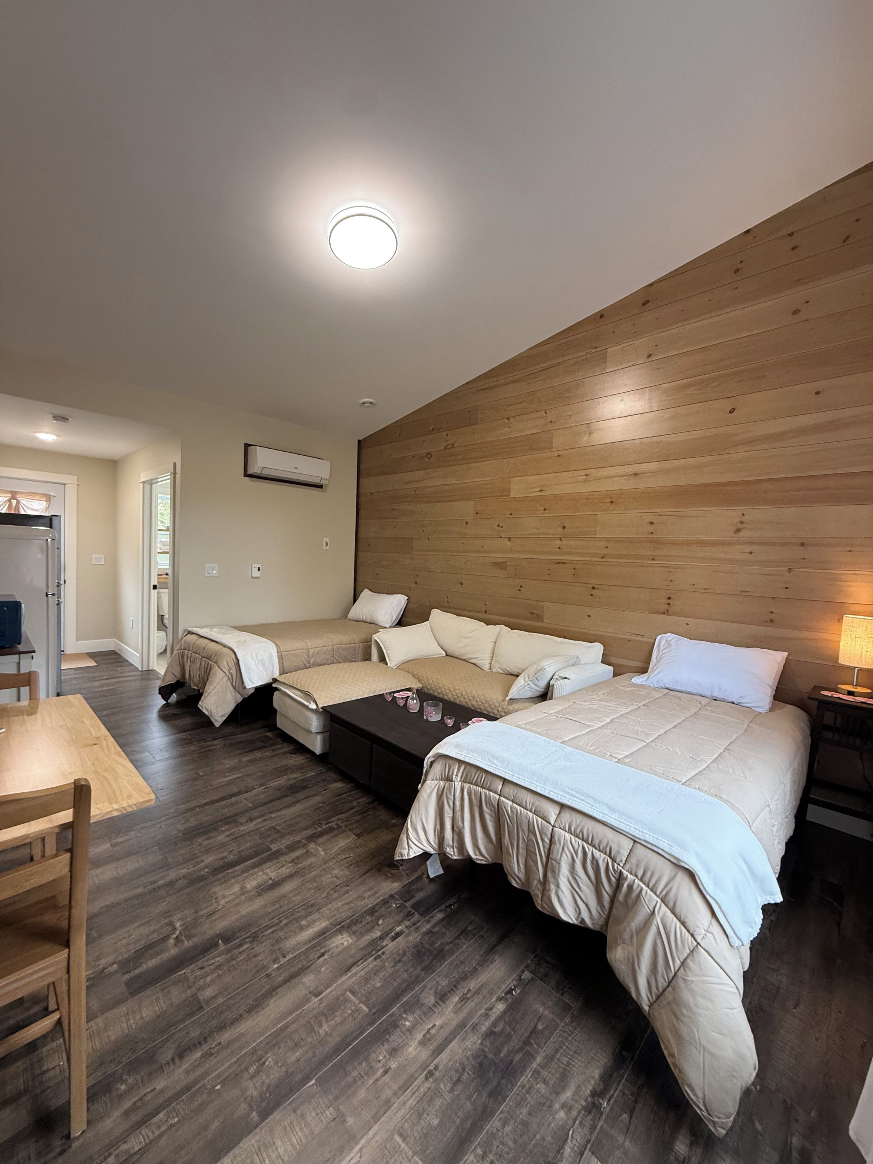 Ein Schlafzimmer mit zwei Betten, einem hölzernen Kopfteil, einem Nachttisch mit Lampe und einem kleinen Tisch mit Getränken.