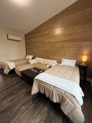 Quarto de hotel com teto de madeira, cama com colcha branca, sofá, mesa pequena com velas e mesa de cabeceira com abajur.