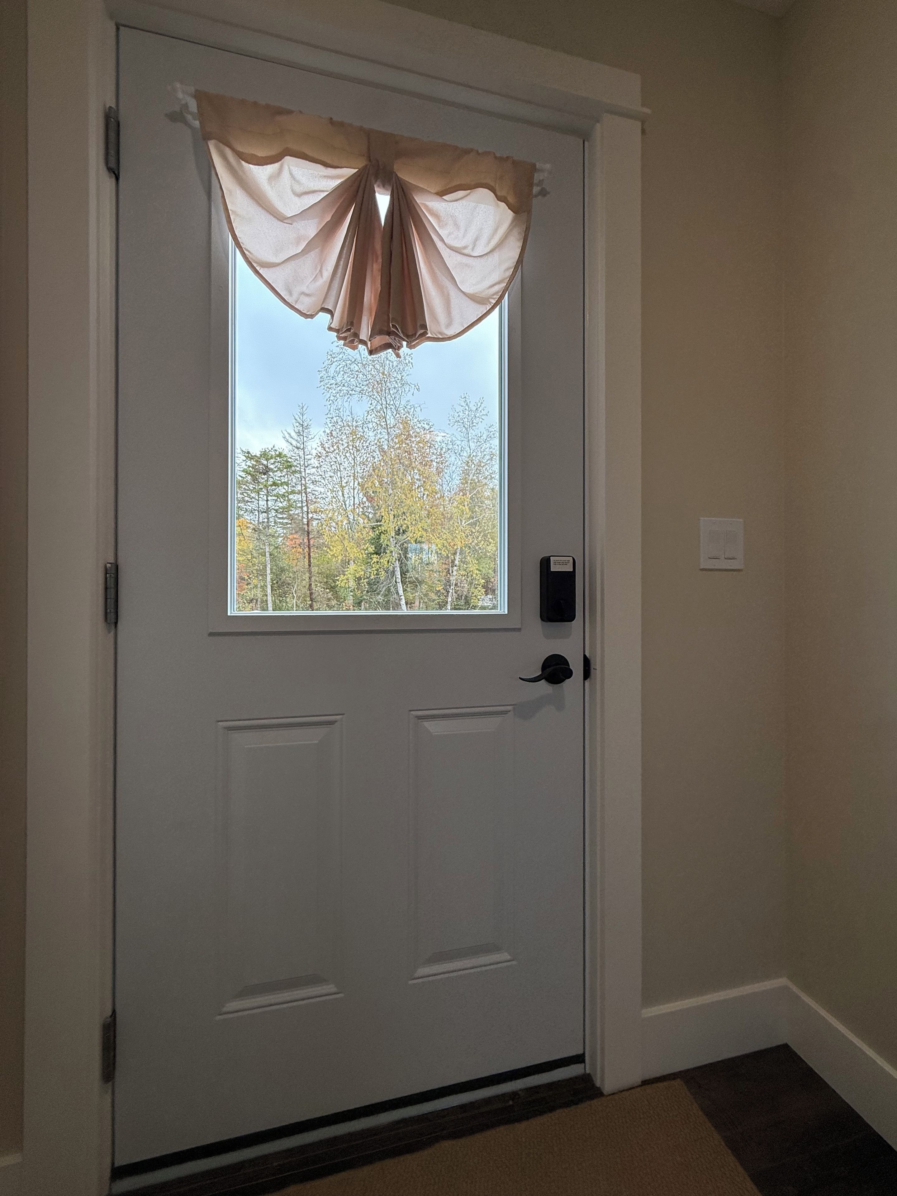 Uma porta branca com janela, um interfone e um interruptor de luz fixado na parede.