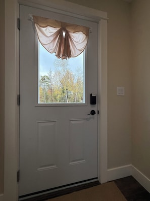 Uma porta branca com janela, um interfone e um interruptor de luz fixado na parede.