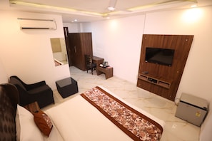 Habitació d'hotel amb llit, televisió penjada a la paret, escriptori amb cadira, nevera petita i mirall.