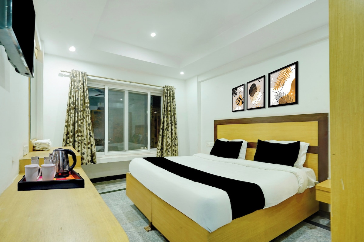 Una habitación de hotel con cama, escritorio con hervidor, ventana con cortinas y tres cuadros en la pared.