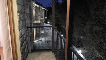 A covered balcony with stone walls, a tiled floor, and a metal railing.