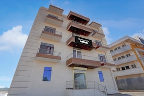 A multi-story building with balconies, a sign indicating it is a serviced company property, and a clear sky. - Townhouse Manipal University Highway (Jaipur)