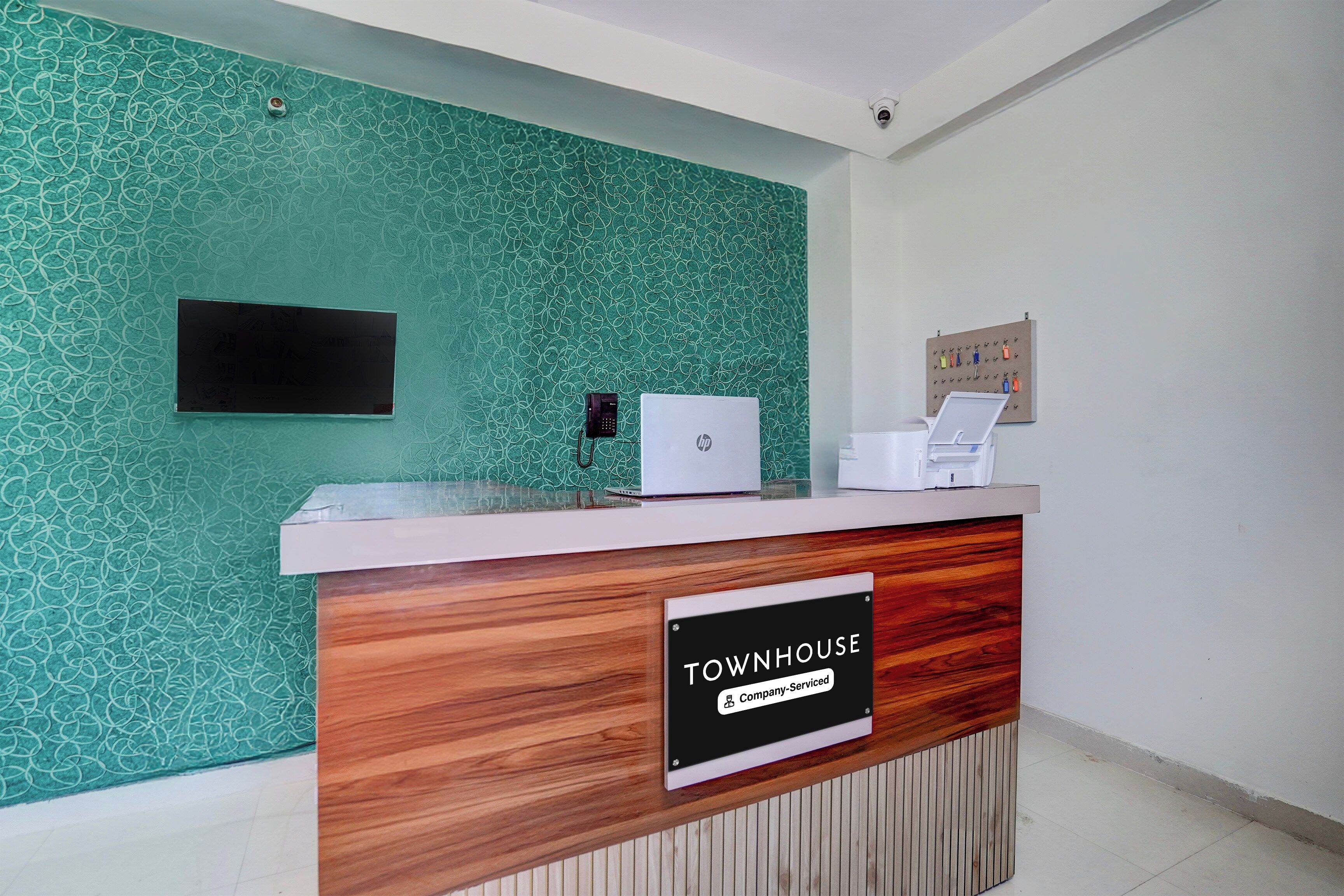 Uma receção com placa 'Townhouse', uma televisão de ecrã plano, telefone e impressora.