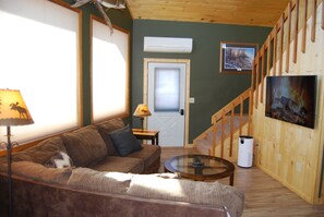 A cozy living room with a sofa, a coffee table, a lamp, and a TV mounted on the wall. - Sapphire Outpost, A Quiet Hilltop Cabin with Stunning Mountain Views (Stevensville)