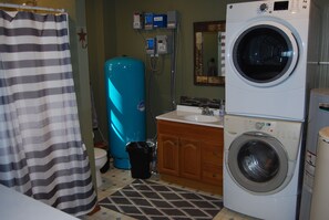 Een kleine badkamer met een gestreept douchegordijn, een blauwe boiler, een wasmachine en een wastafel.