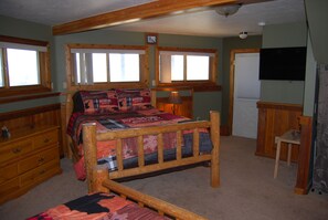 A bedroom with a wooden bed, a dresser, a chair, and a television on the wall. - Sapphire Outpost, A Quiet Hilltop Cabin with Stunning Mountain Views (Stevensville)