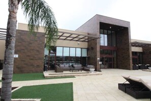 A modern building with a glass entrance, outdoor seating area, and artificial grass. - 3212 Magic Village 8 Guests Lakefront 8 min Disney (Kissimmee)