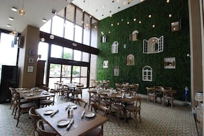 A restaurant with wooden tables and chairs, large windows, and a green wall with window designs. - 3212 Magic Village 8 Guests Lakefront 8 min Disney (Kissimmee)