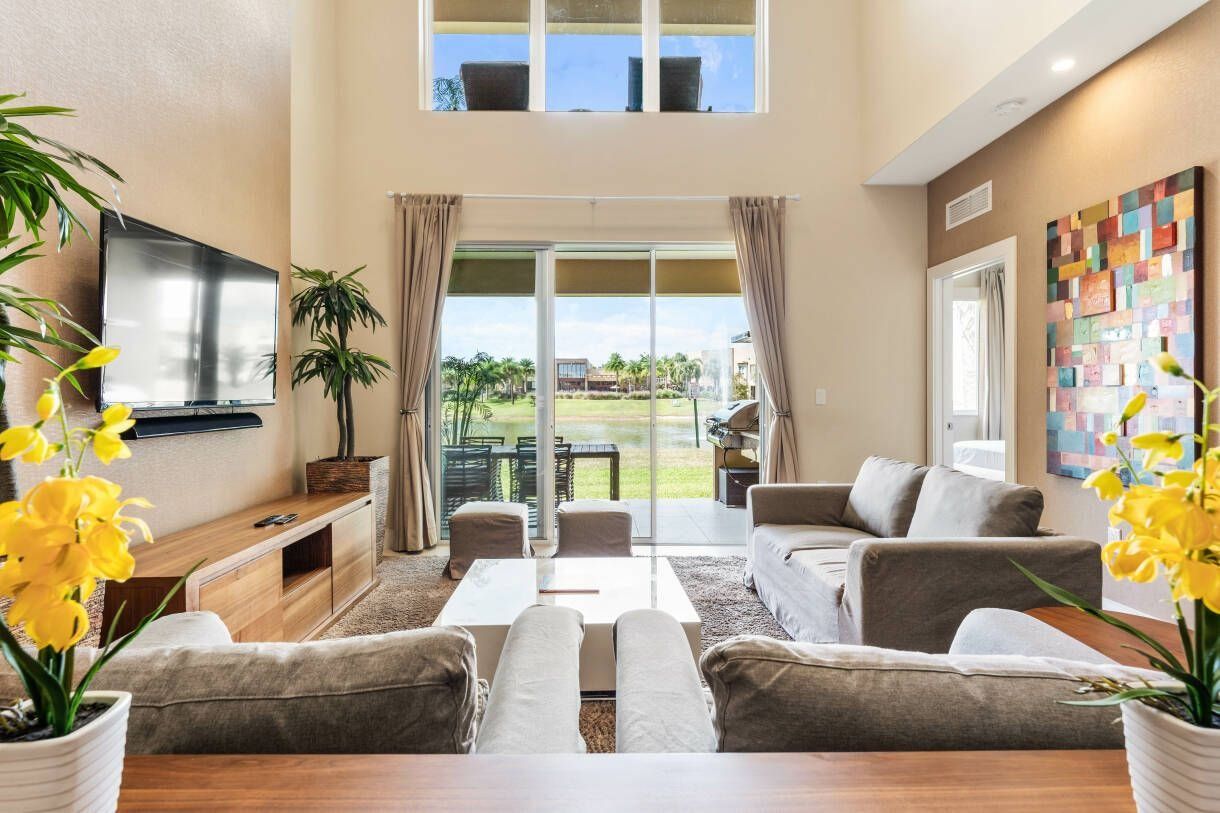 A spacious living room with a flat-screen TV, comfortable seating, a coffee table, and a large sliding glass door leading to a balcony.