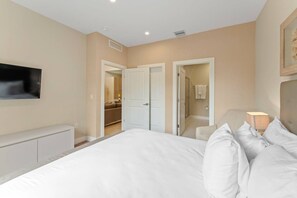 A bedroom with a bed, a TV mounted on the wall, and a door leading to a bathroom. - 3212 Magic Village 8 Guests Lakefront 8 min Disney (Kissimmee)
