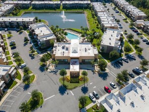 An aerial view of a residential complex with multiple apartment buildings, a central courtyard with a fountain, and a swimming pool. - 3212 Magic Village 8 Guests Lakefront 8 min Disney (Kissimmee)
