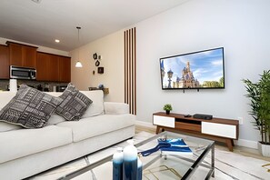 A modern living room with a sofa, coffee table, and a flat-screen TV mounted on the wall. - 4BR w/ Pool + Mickey & Harry Potter Themes (Kissimmee)