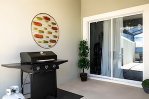 Eine Terrasse mit Grill, einer dekorativen Wandgestaltung, einem Blumentopf und einer Glastür zum Balkon.