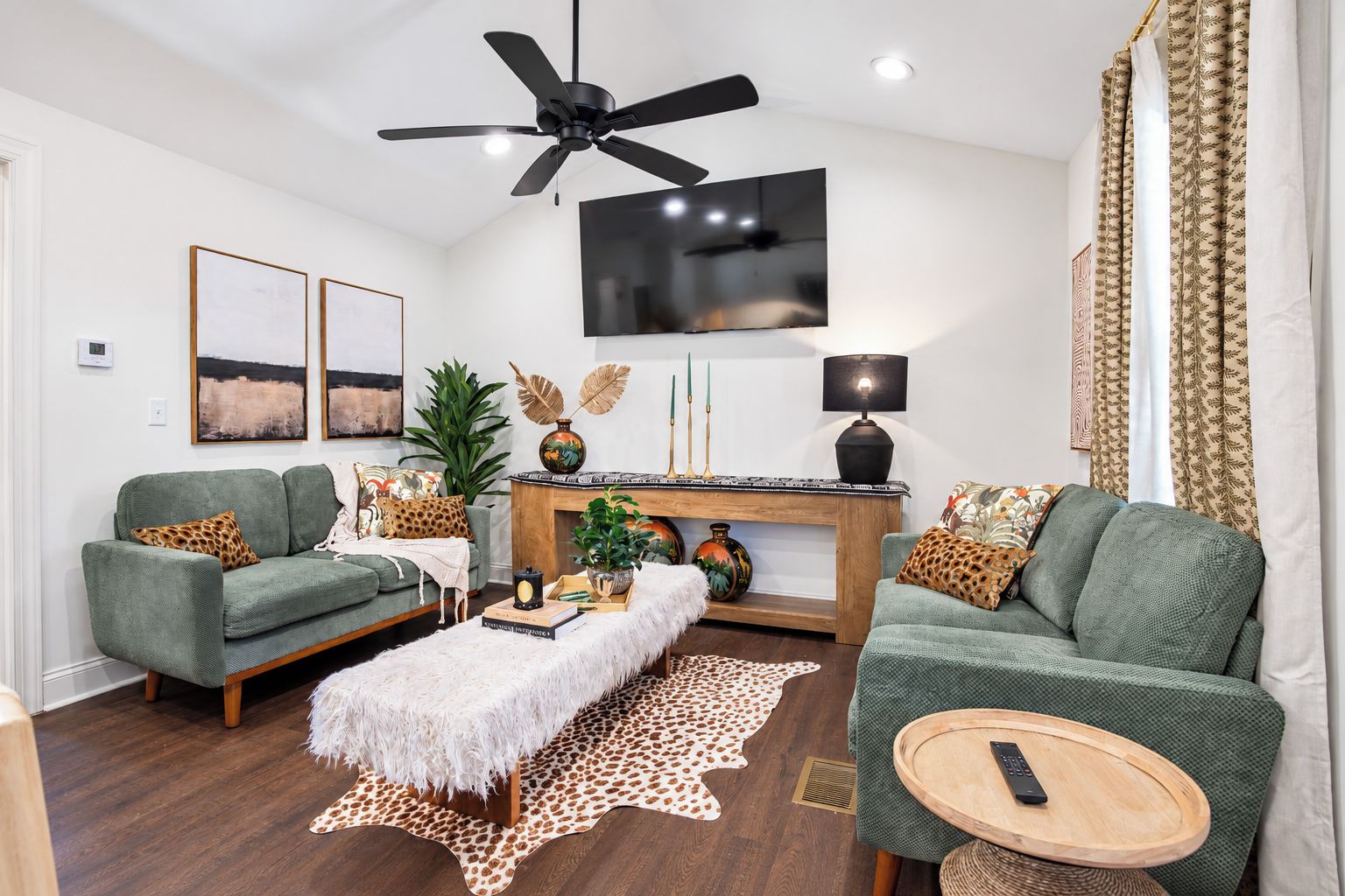 A modern living room with two green sofas, a white furry ottoman, a wooden coffee table, and a fireplace with decorative items.