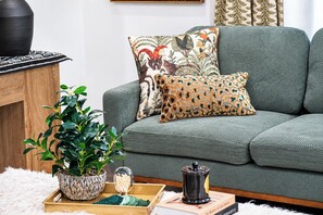 A living room with a grey sofa, a patterned throw pillow, a potted plant, a decorative glass jar, and a book. - The Freddy, Near the Square by Velvet Ditch Villas (Oxford)