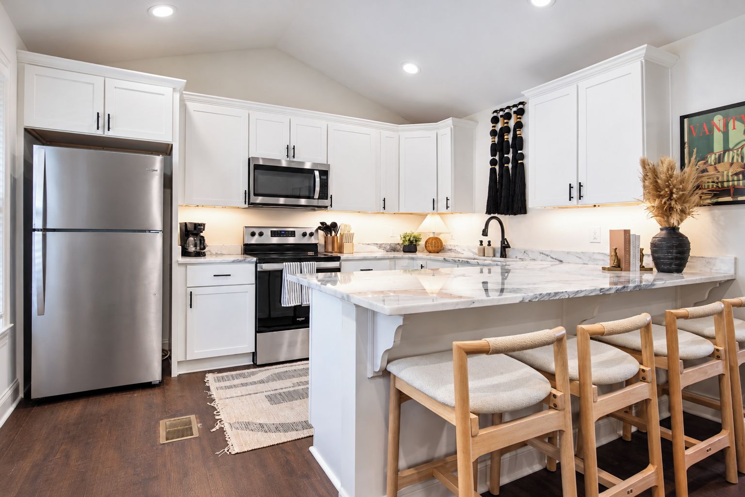 A modern kitchen with white cabinetry, stainless steel appliances, a marble countertop, and a bar stool seating area.