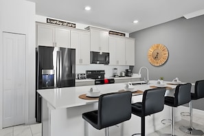 Una cocina moderna con armarios blancos, electrodomésticos de acero inoxidable y una isla central con taburetes de bar.