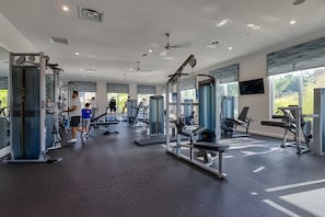 Un gimnasio moderno con diversos equipos de ejercicio, ventanas amplias y un techo alto.