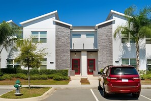 A modern building with a symmetrical facade, two red doors, and a parking area with a red car. - Disney 4BR w/ Pool + Themed Rooms in Storey Lake (Kissimmee)