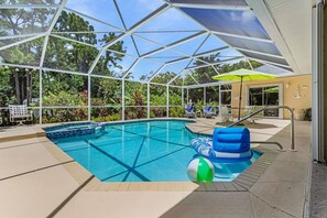 A covered swimming pool with a glass ceiling, surrounded by lounge chairs and umbrellas. - Pineapple Paradise Retreat Private Pool and Spa (Bonita Springs)
