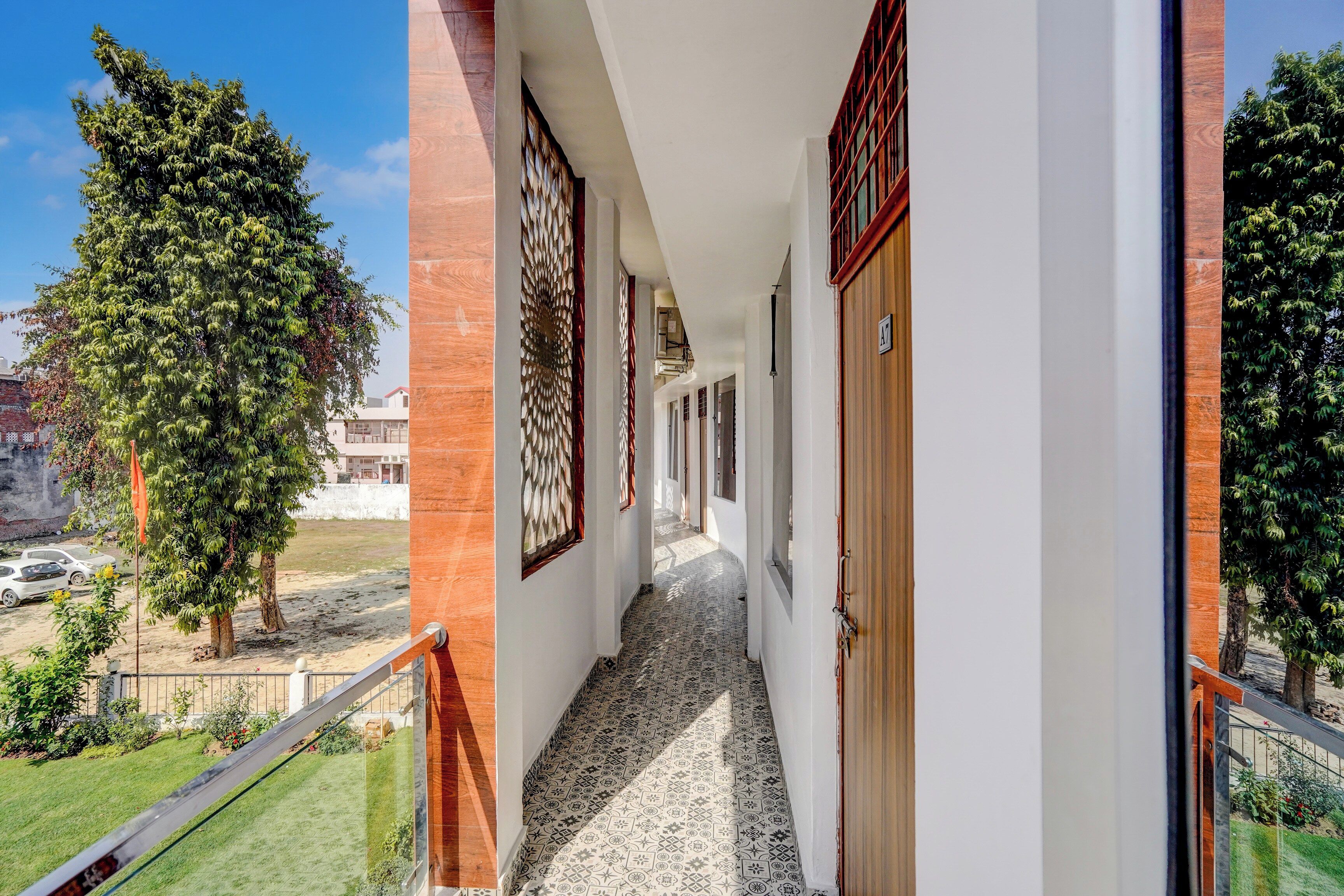 Passadís amb sòl estampat, una porta de fusta i vista a arbres i edificis.