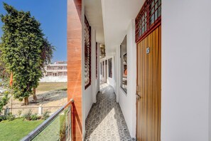 A corridor with a patterned floor, a wooden door, and a view of a building in the background.
