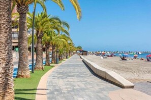 Eine Strandpromenade mit Palmen, einem Sandstrand und Strandsonnenschirmen.
