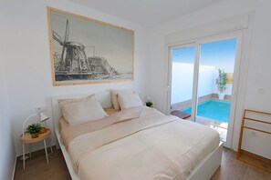 Quarto com cama, mesa de cabeceira, quadro e vista para uma piscina.