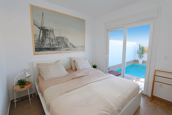 A bedroom with a bed, a nightstand, a painting, and a view of a swimming pool. - Molino Beach House - San Pedro del Pinatar (San Pedro del Pinatar)