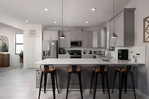 A modern kitchen with a large island, bar stools, stainless steel appliances, and pendant lighting. - 6BR Storey Lake Villa w/ Pool, Spa & EV Charger (Kissimmee)
