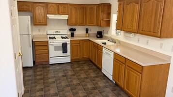 A kitchen with wooden cabinets, a white stove, a dishwasher, and a tiled floor.