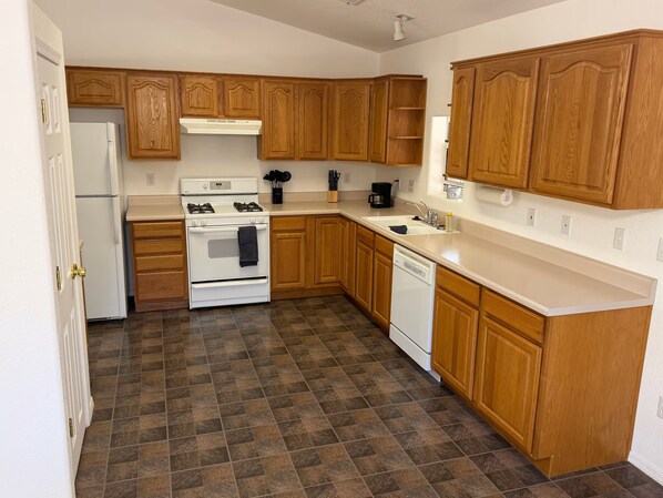 Una cocina con armarios de madera, estufa blanca, lavavajillas y piso de baldosas.