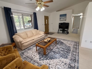 A living room with a beige sofa, a patterned rug, a coffee table, and a ceiling fan.