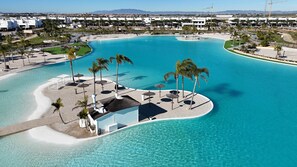 An aerial view of a resort with a large, curved swimming pool surrounded by palm trees and lounge chairs. - Residencial Exclusive - Santa Rosalia Lake Resort (Torre-Pacheco)