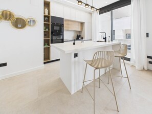 A modern kitchen with a central island, bar stools, and built-in appliances. - Residencial Exclusive - Santa Rosalia Lake Resort (Torre-Pacheco)
