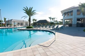 A swimming pool with sun loungers and a covered seating area, surrounded by palm trees and a building with a flat roof. - Luxury 6BR Villa w/ Pool, Spa & Near Disney (Kissimmee)