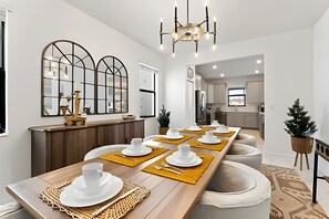 A modern dining area with a long wooden table set for six, white plates, and gold placemats. - Luxury 6BR Villa w/ Pool, Spa & Near Disney (Kissimmee)