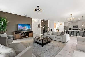 A modern living room with a flat-screen TV, a glass coffee table, and a sofa. - Luxury 6BR Villa w/ Pool, Spa & Near Disney (Kissimmee)